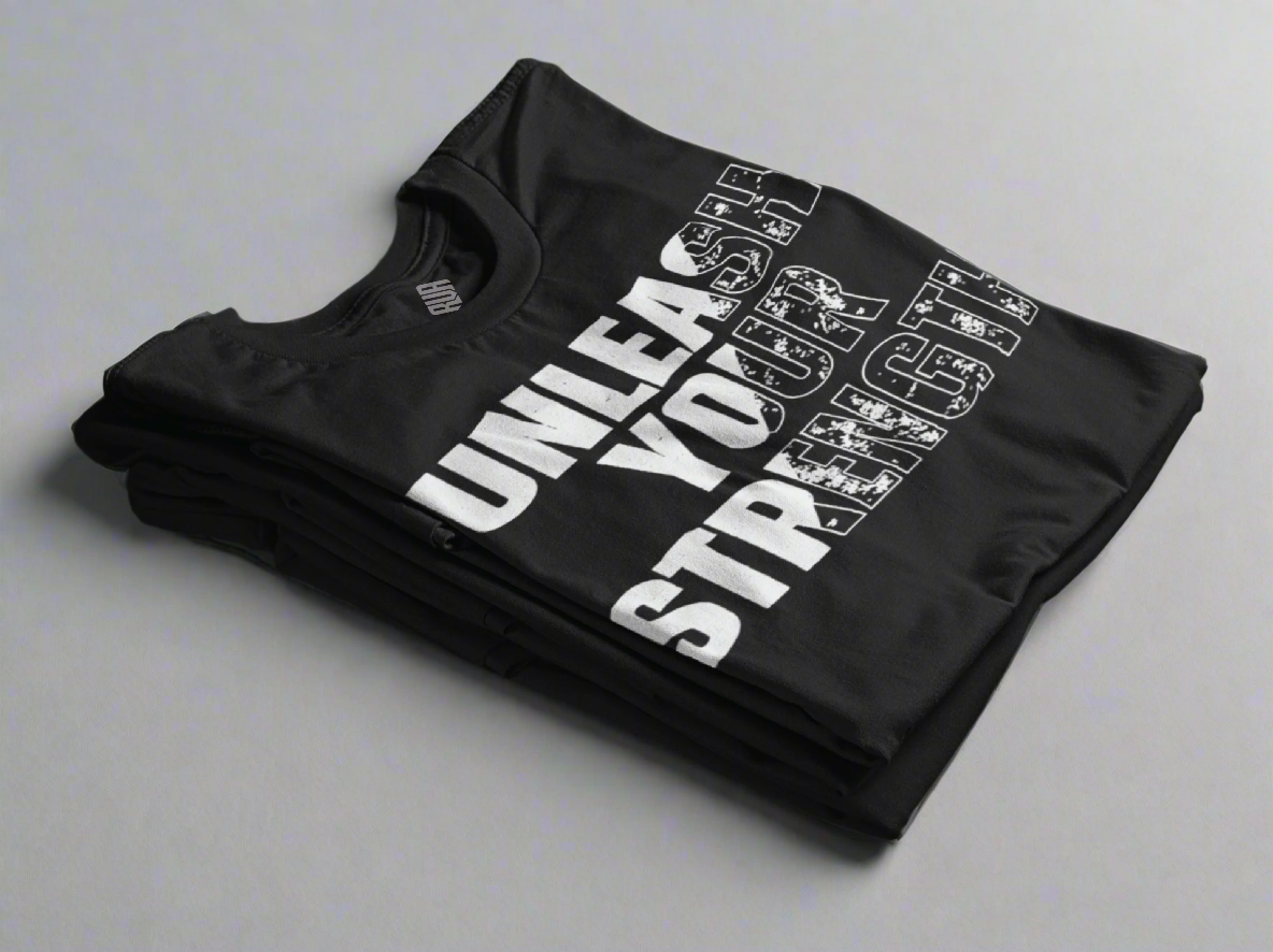 Black Unleash Your Strength T-shirt neatly folded, showcasing its bold design. This empowering and comfortable tee is perfect for those who embrace resilience and confidence in their everyday journey.