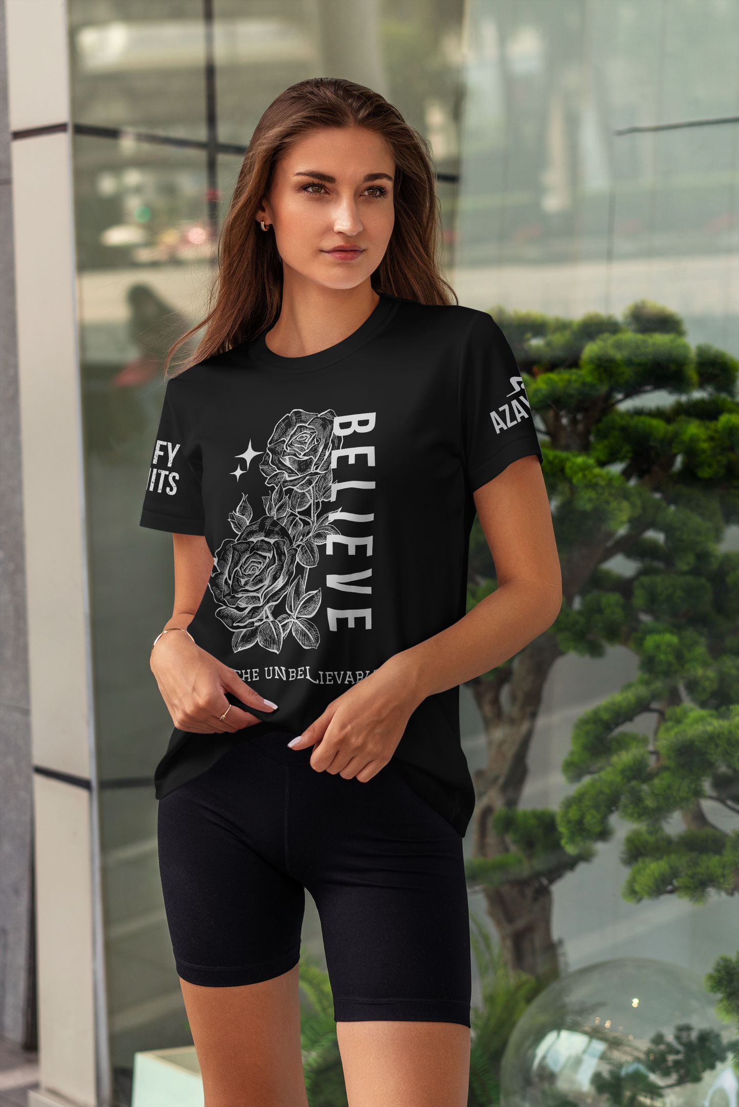 Woman wearing a black t-shirt with graphic design and text, standing in front of a glass wall.