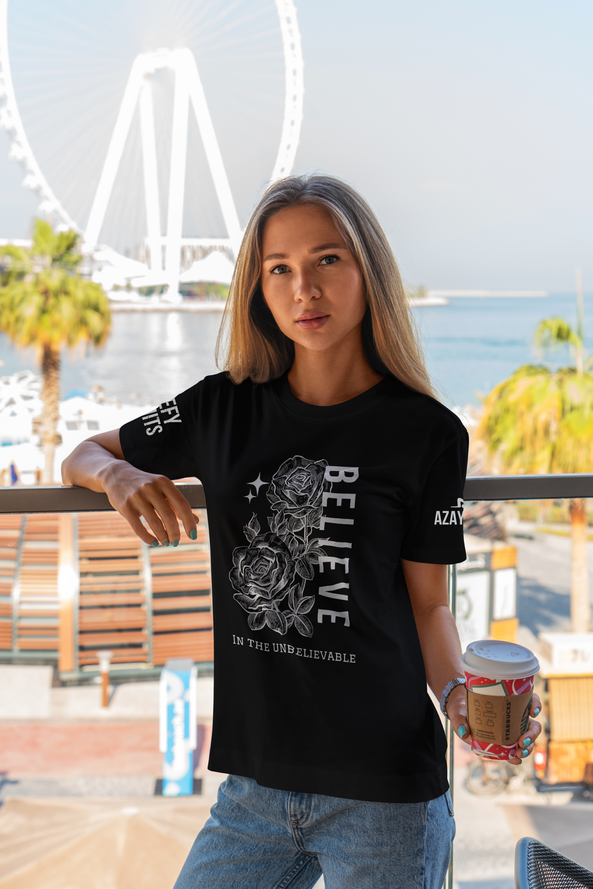 Woman wearing a black t-shirt with a design and text, holding a coffee cup outdoors.