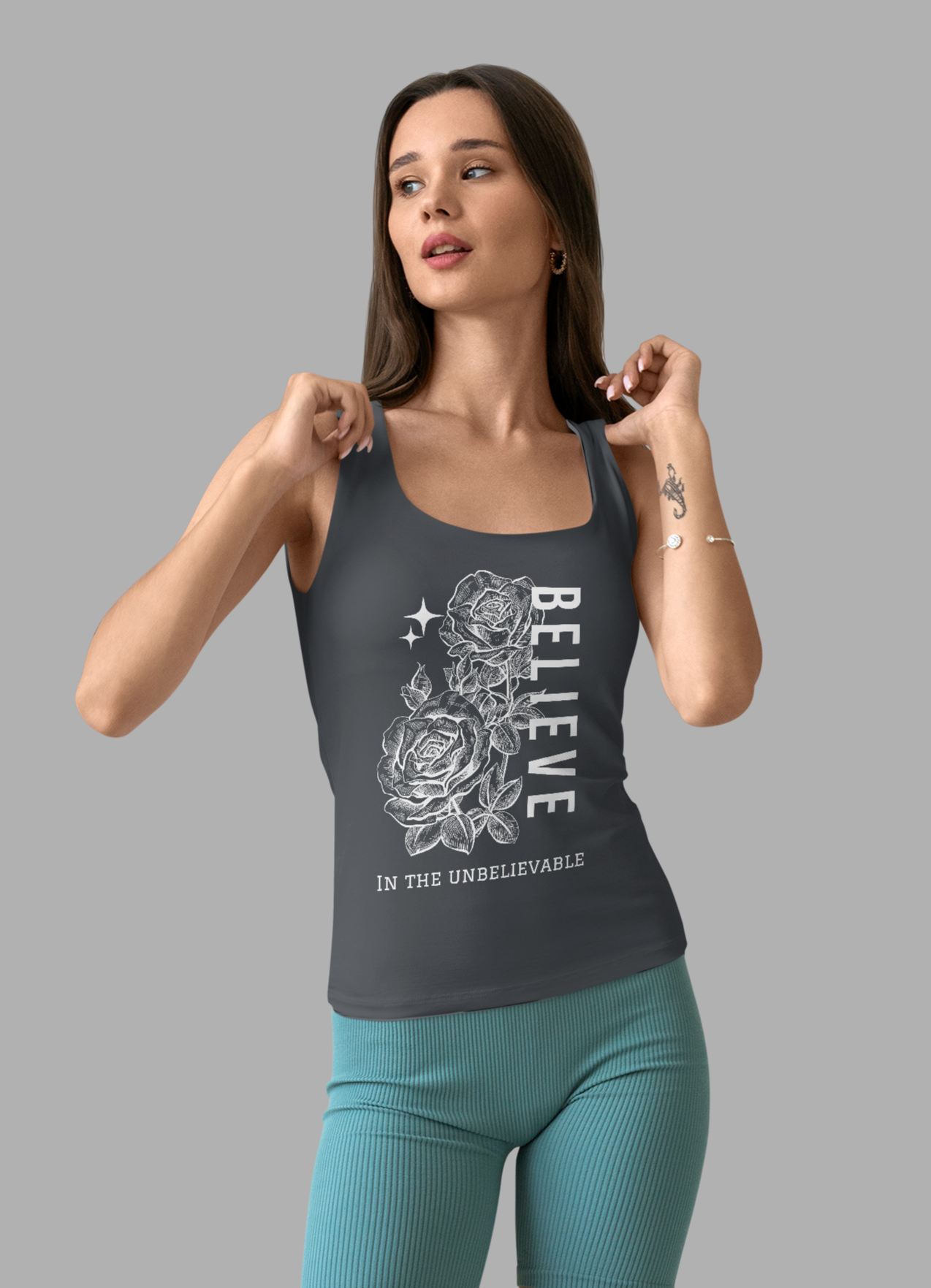 Woman wearing a gray tank top with a graphic design and teal shorts on a gray background