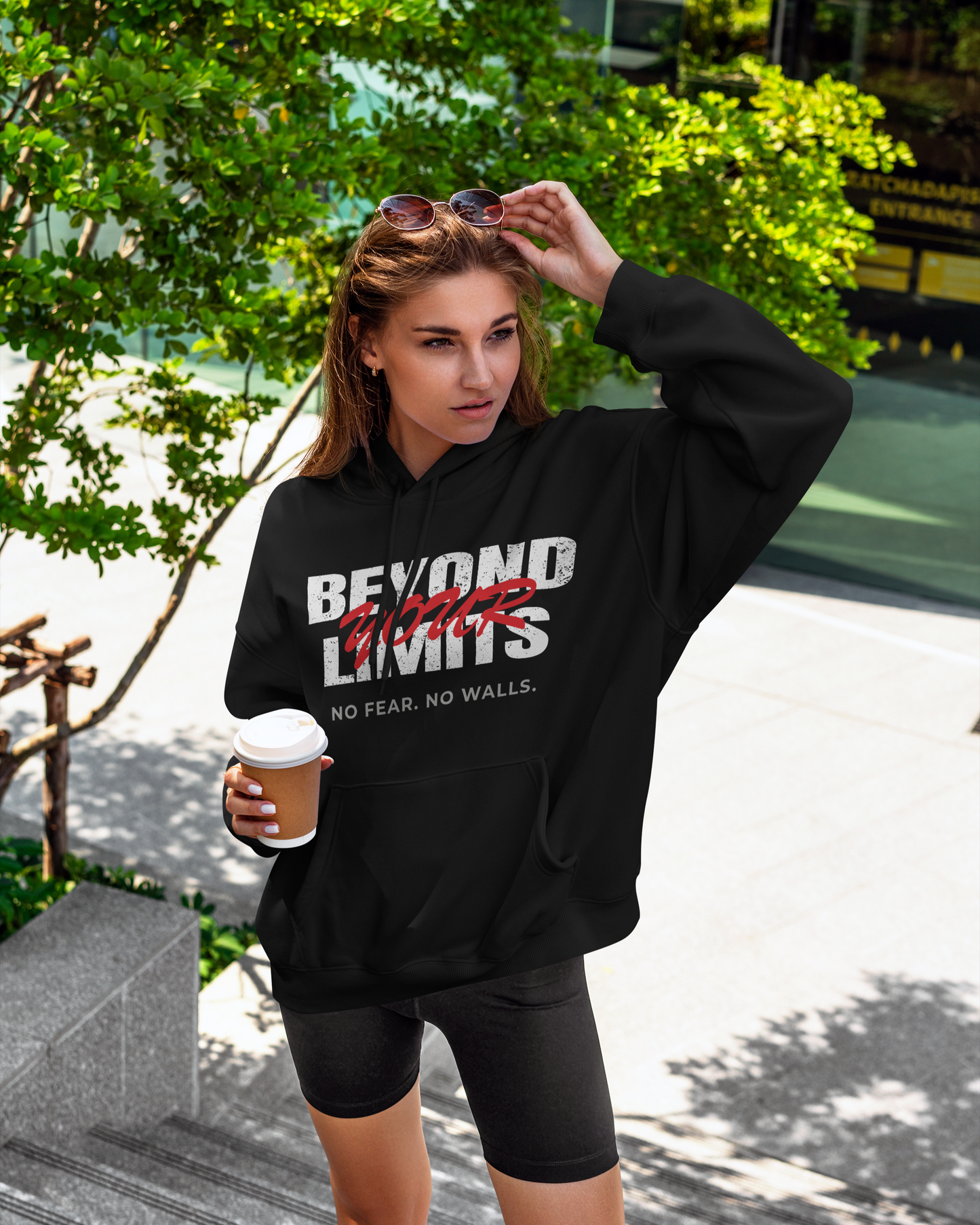 women walking in the park holding coffee wearing black hoodie with text beyond your limits