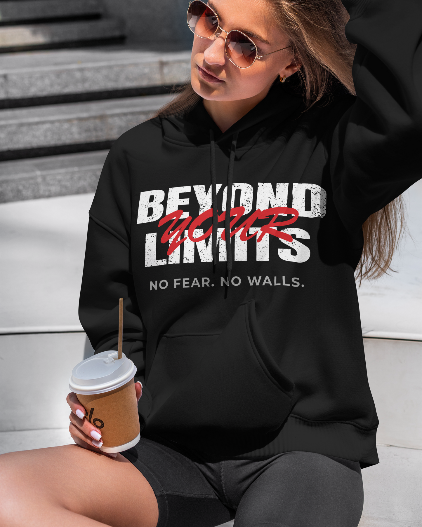women sitting on step holding coffee wearing black hoodie with text beyond your limits