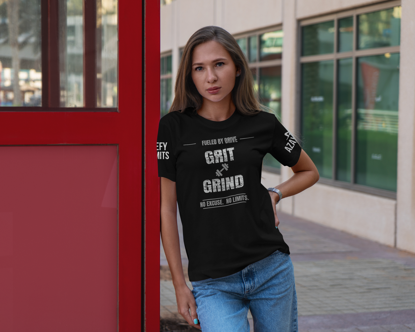 model wearing black tee with the text grit and grind leaning against a red door