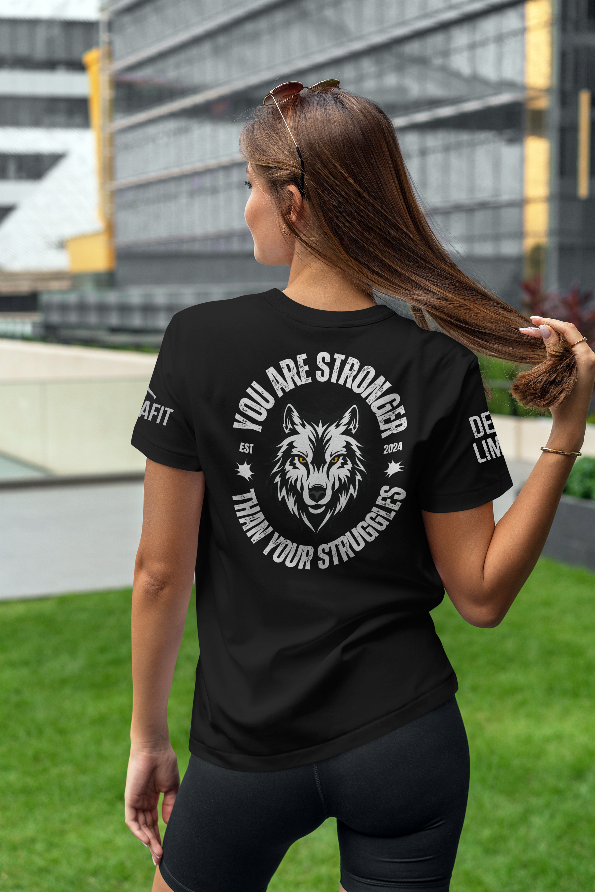 Woman wearing a black t-shirt with a wolf graphic and motivational quote outdoors.