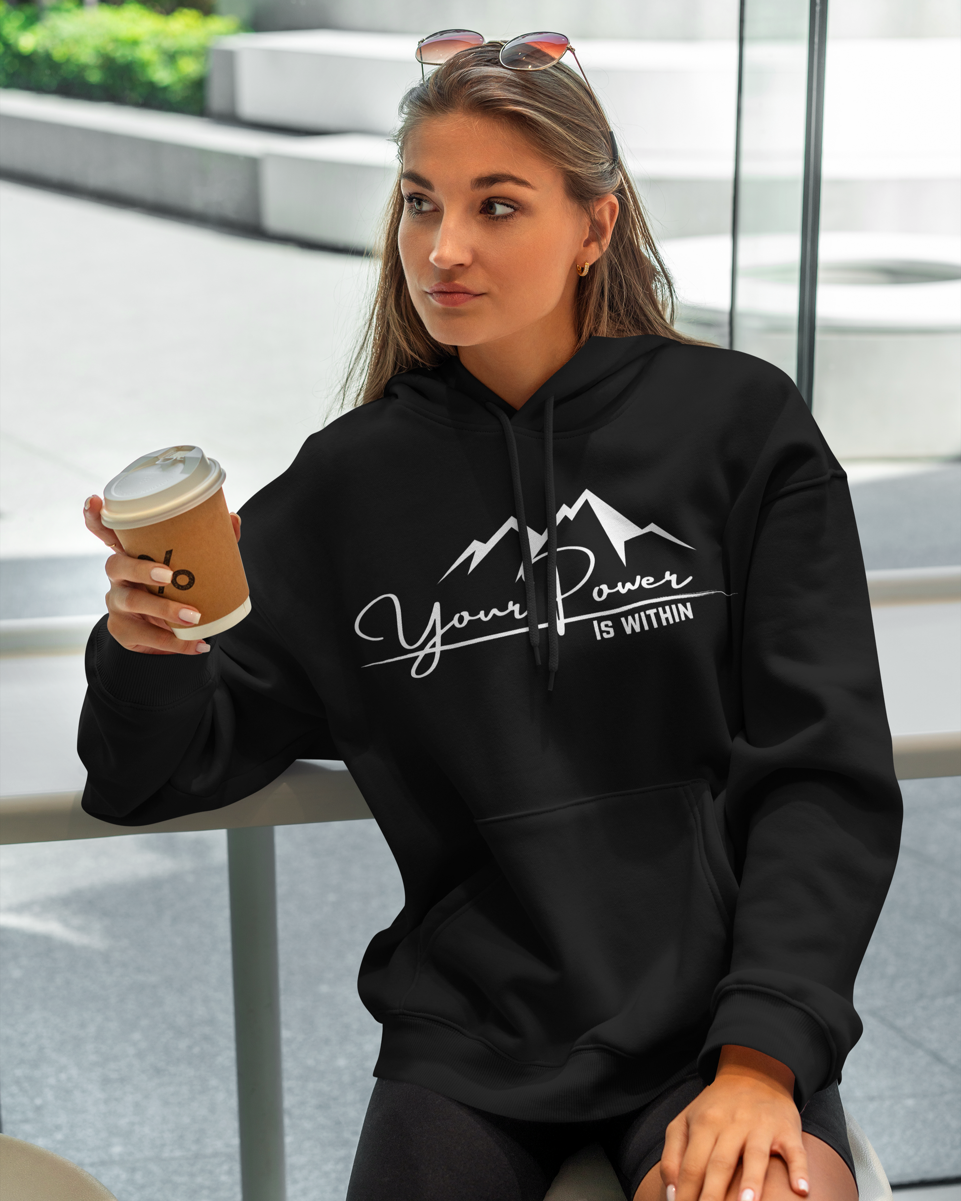 Woman wearing a black hoodie with 'Your Power is Within' text, holding a coffee cup.