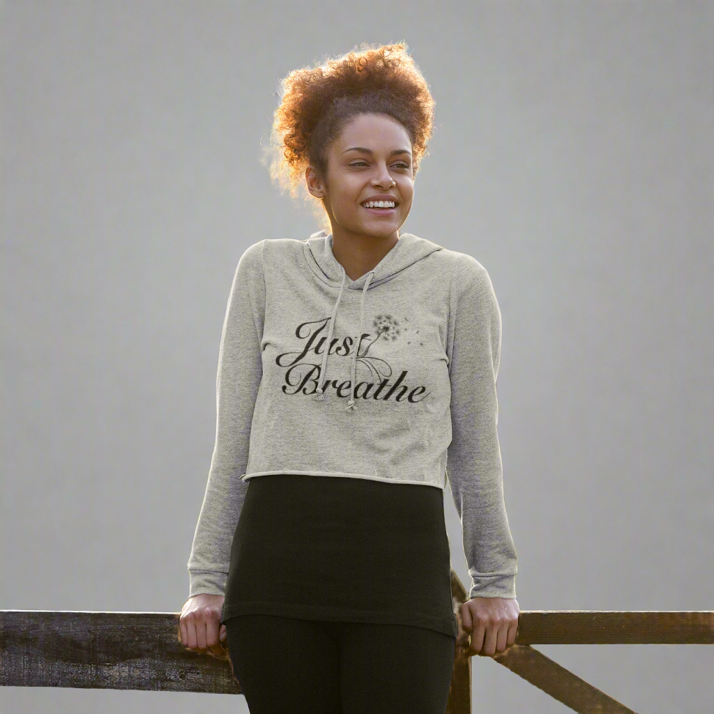 Happy woman leaning on a wooden fence while wearing the heather grey Just Breathe crop hoodie, a stylish and comfortable choice for casual wear and workouts.