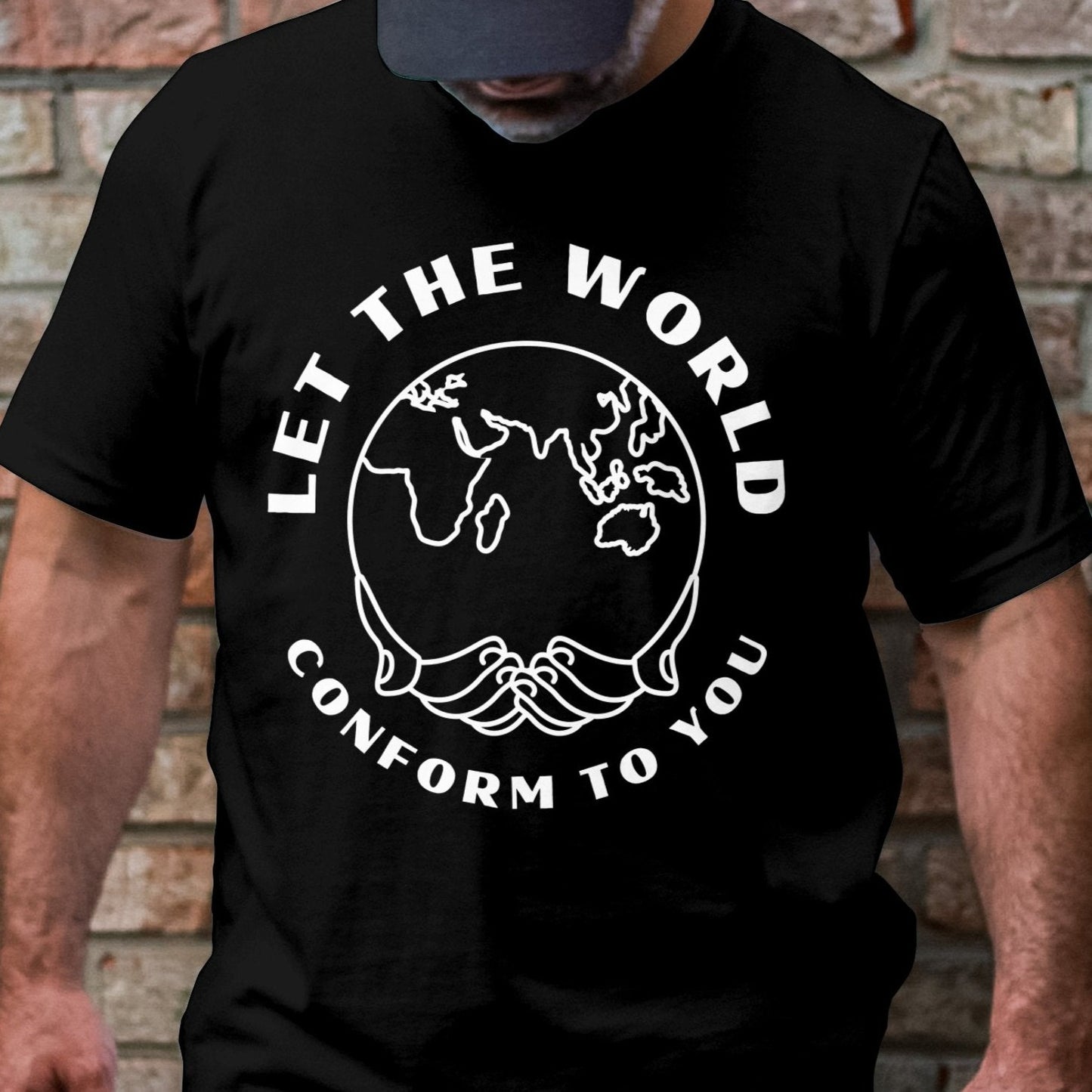 Cropped image of a bearded man looking down while leaning against a brick wall, wearing a black T-shirt with the "Let the World Conform to You" design in white text surrounding a world outline.