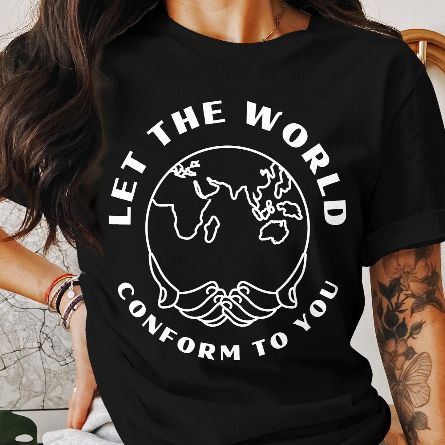 Cropped image of a female model wearing a black T-shirt with the "Let the World Conform to You" design, featuring white text surrounding a world outline.