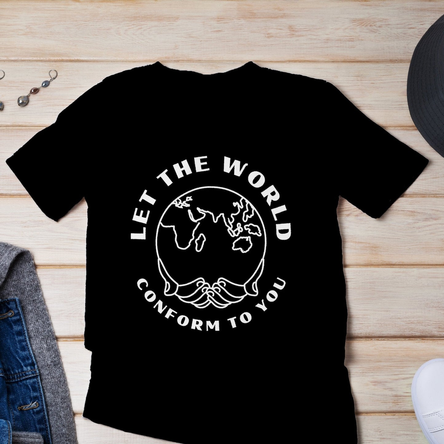 Black T-shirt featuring the "Let the World Conform to You" design laid flat on a wooden plank, highlighting the white text and world outline graphic. The natural wood texture contrasts with the bold design.