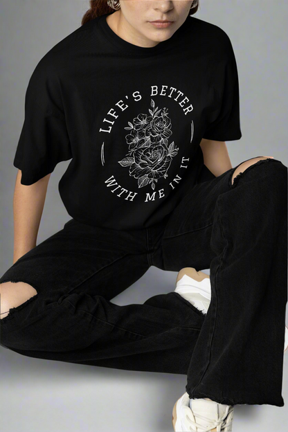 Woman sitting in a studio while wearing the Life Is Better With Me In It black T-shirt, showcasing its uplifting message and comfortable oversized fit.
