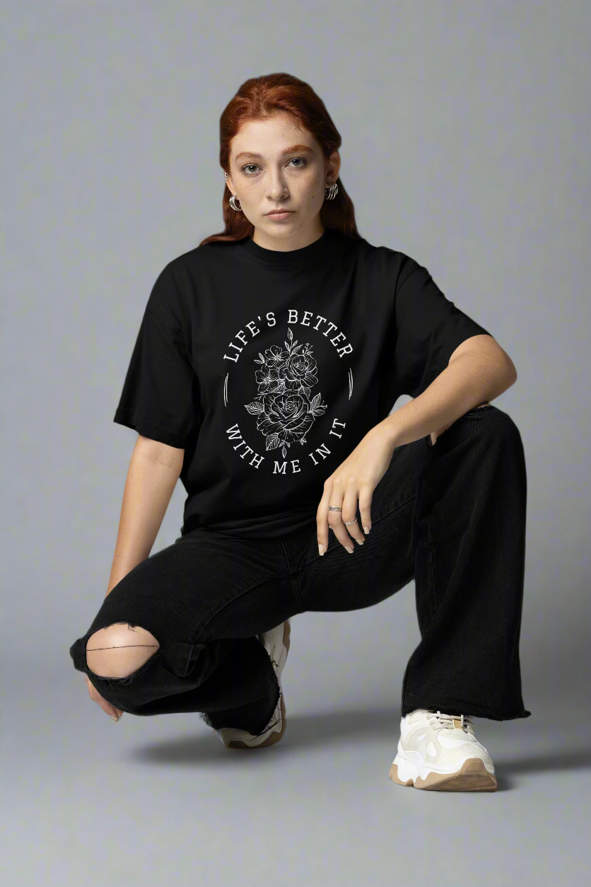 Woman squatting in a studio while wearing the Life Is Better With Me In It black T-shirt, showcasing its uplifting message and comfortable fit.