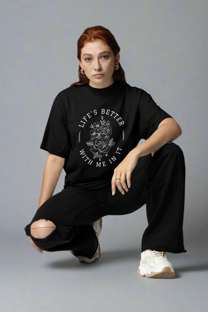 Woman squatting in a studio while wearing the Life Is Better With Me In It black T-shirt, showcasing its uplifting message and comfortable fit.