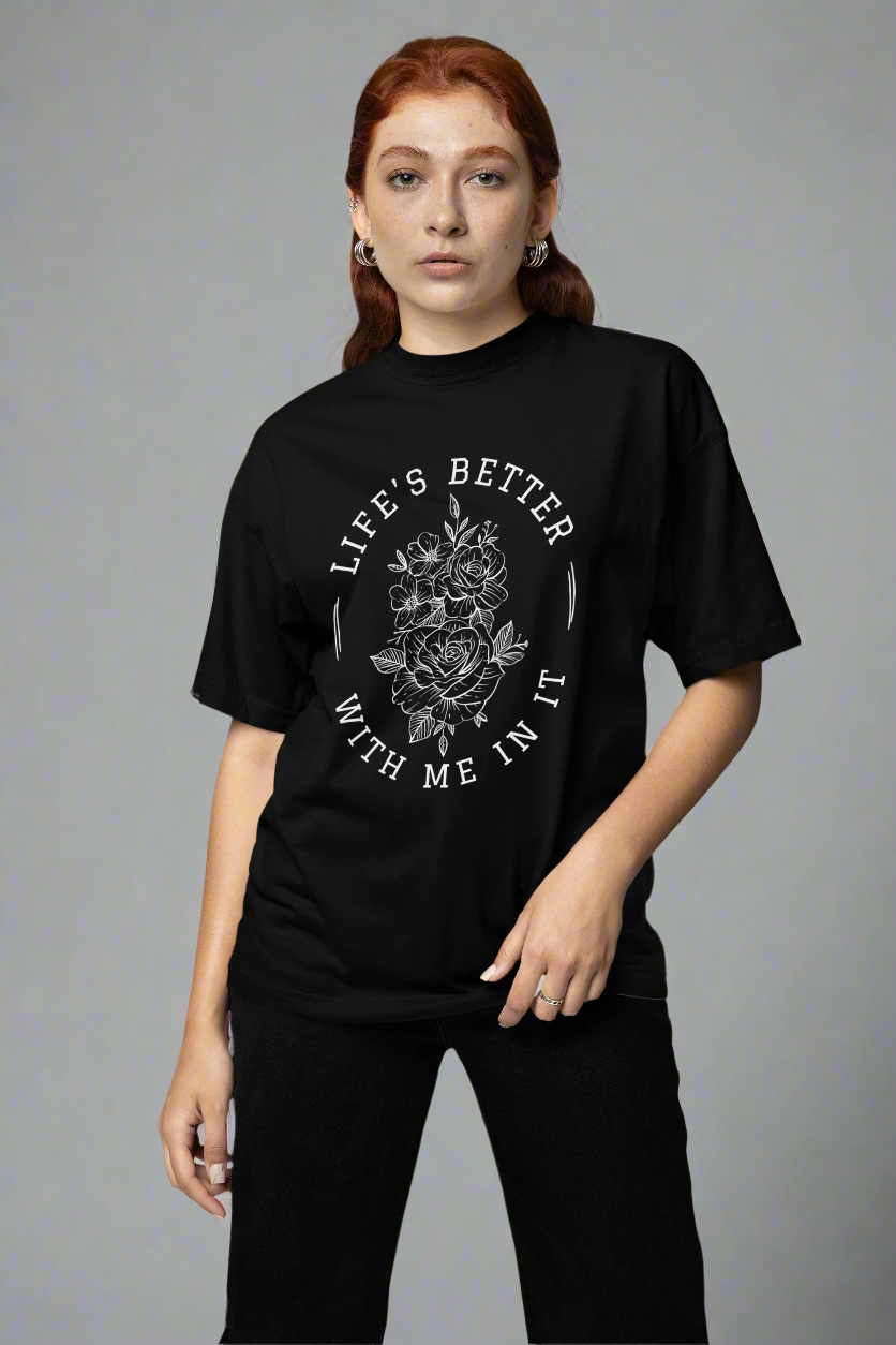 Woman standing in a studio wearing the Life Is Better With Me In It T-shirt, showcasing a meaningful and uplifting design.