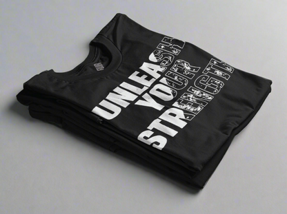 Black Unleash Your Strength T-shirt neatly folded, showcasing its bold design. This empowering and comfortable tee is perfect for those who embrace resilience and confidence in their everyday journey.