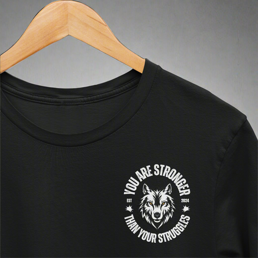 You Are Stronger T-shirt with a small left chest wolf design, displayed on a wooden hanger against a wall, representing strength and resilience.